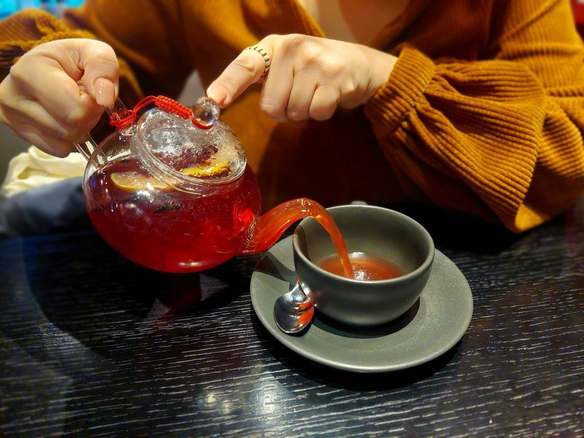 A steaming cup of red clover tea beside fresh herbs and flowers